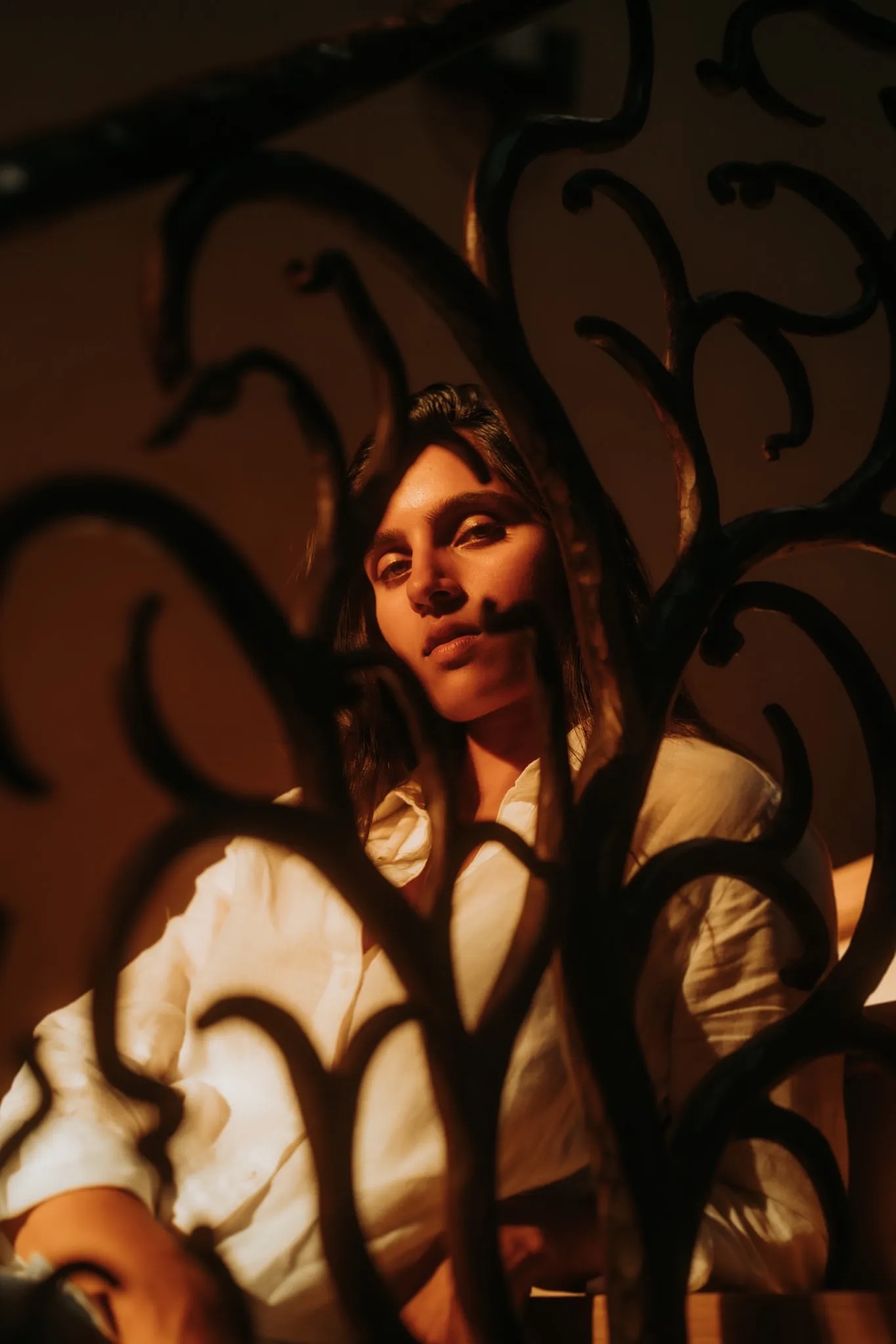 Close up of Diya Patel leaning against a staircase in amber light looking at the camera